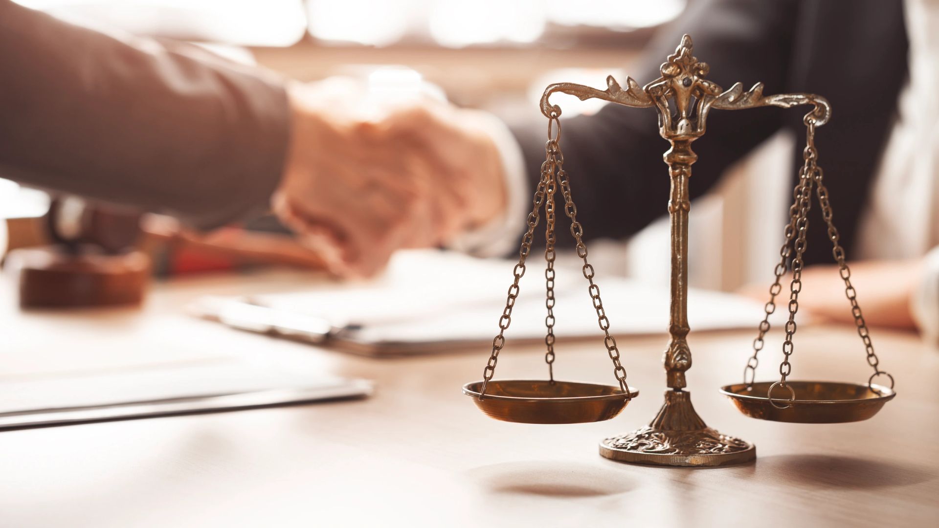 Scales of justice on a desk as attorney and client shake hands